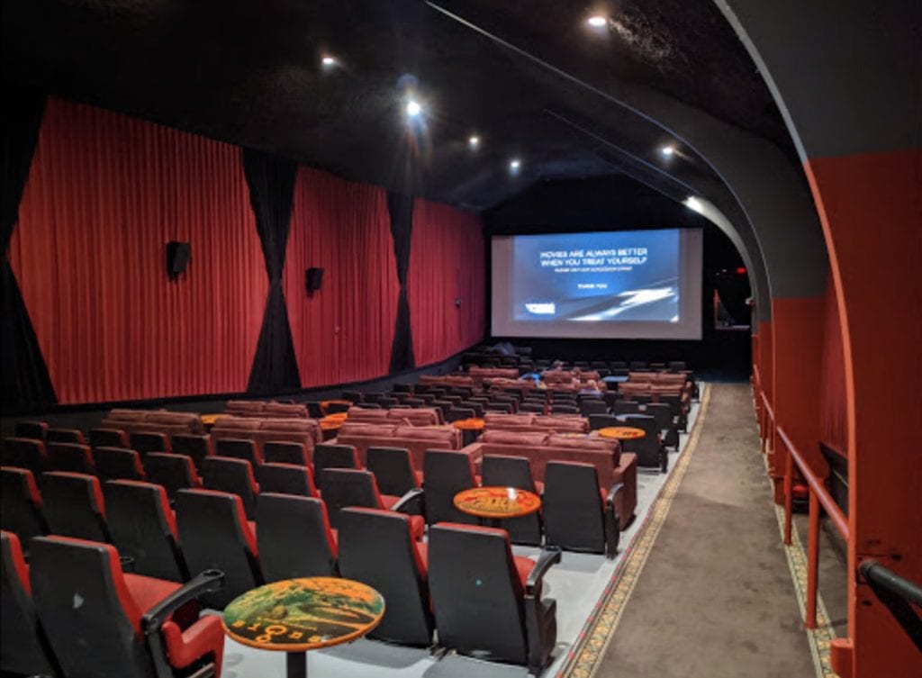 Red velvet seats and small cocktail tables facing a movie screen at Vine Cinema & Alehouse in Livermore.